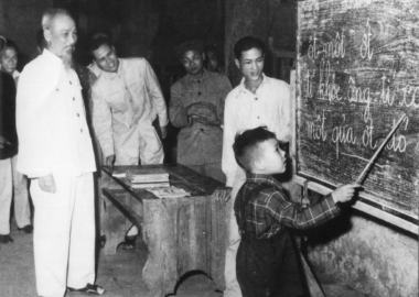 Bác Hồ quan sát một cháu thiếu nhi tập đánh vần khi đến thăm lớp học vỡ lòng Đình Thạch Khối ở phố Hàng Than, Hà Nội (31/12/1958)